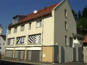 Ein helles Wohnhaus mit rotem Ziegeldach. Im Erdgeschoss befinden sich mehrere Garagentore.